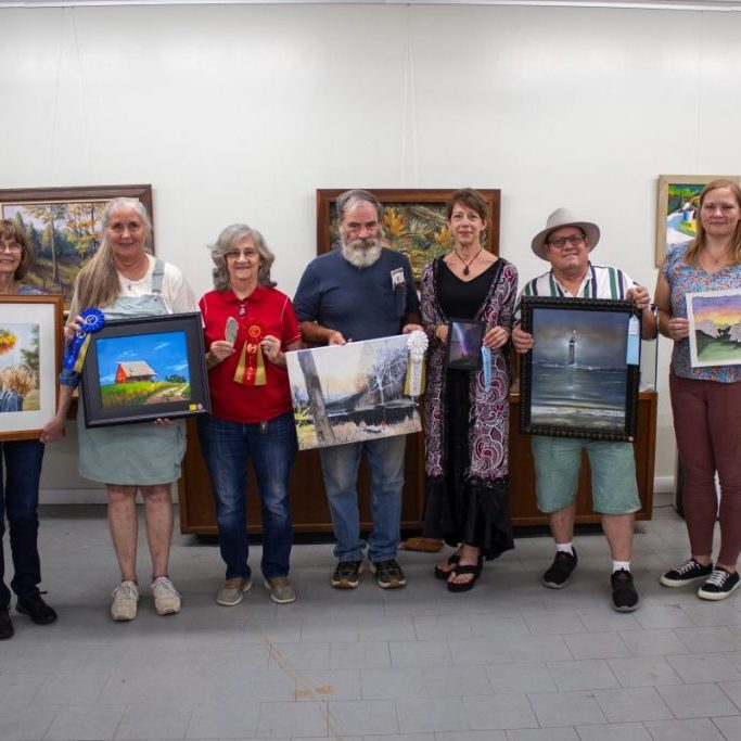 Photo by Shari Harris
In the adult category, from left, Ellen Reynolds won the People’s Choice award, Patty Burmeister’s painting took first place, Jo Ennis’ rock carving won second place, Robert Shank earned a third place ribbon with his outdoor scene, Brenda Kaiser’s night sky earned honorable mention, Chuck Roling’s lighthouse painting was chosen for honorable mention, and Kierra Lonning’s work received honorable mention. All the works on display were exemplary, and the judges had a difficult time choosing the winners.
